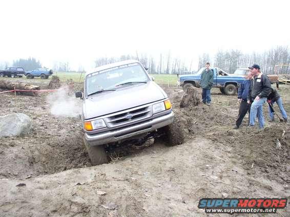 Silver pickup truck with a grille from the 1990s stuck in a mud pit