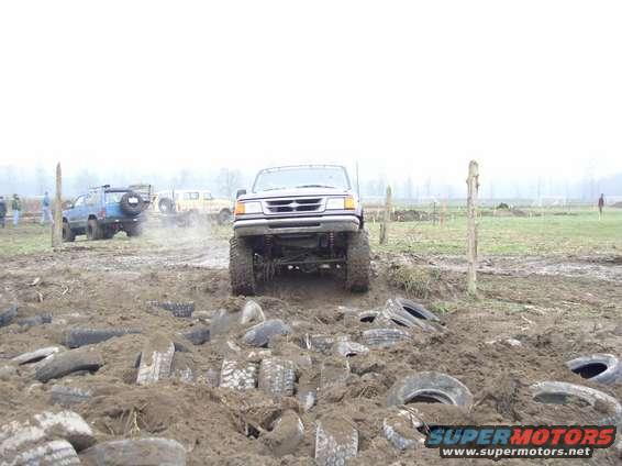 Off-road trucks navigating a muddy obstacle course with tires scattered