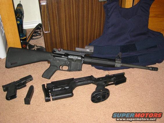 AR-15 style rifle, pistol, drum magazine, and body armor laid out on carpet