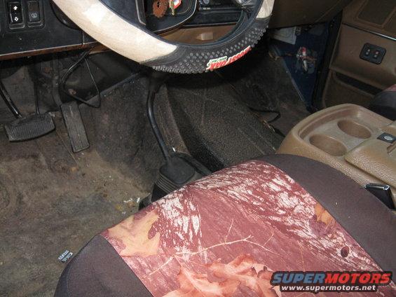 Interior view of a vehicle showing pedals, steering wheel cover, and camouflage seat cover
