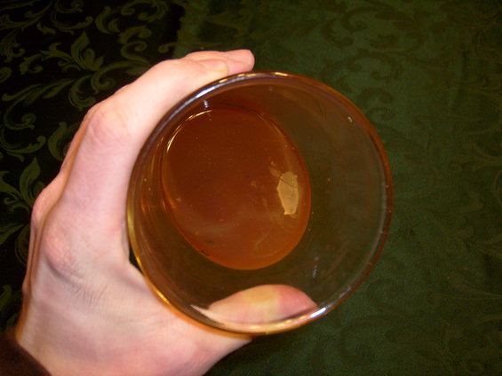 Hand holding a glass of amber liquid over a dark green patterned tablecloth