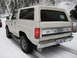 1980 Ford Bronco - A white 1980 Ford Bronco drives through snow-covered terrain, with a red vehicle partially visible on the left.