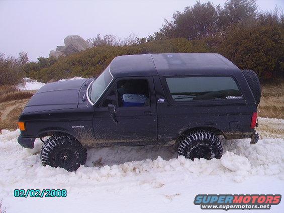Black 1990 Ford Bronco with large tires stuck in snow, side view