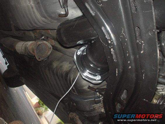 Underbody view of exhaust pipe and suspension parts. A white wire is visible