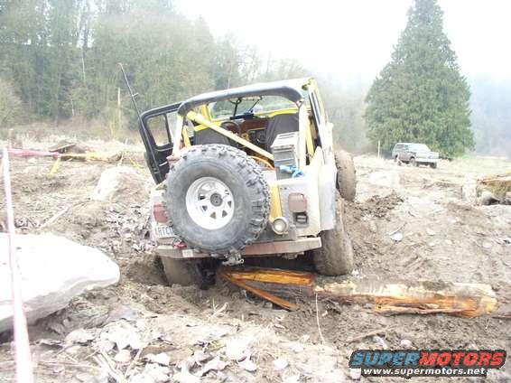 Yellow off-road vehicle stuck in mud, rear view with spare tire