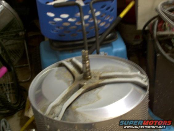Washing machine drum with a metal agitator shaft and a blue laundry basket in the background