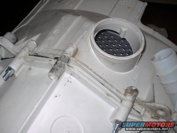 Close-up of a white plastic washing machine component with metal fasteners and a perforated filter inside a tube