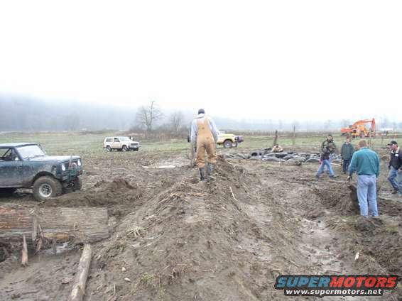 Muddy off-road scene with multiple vehicles and people