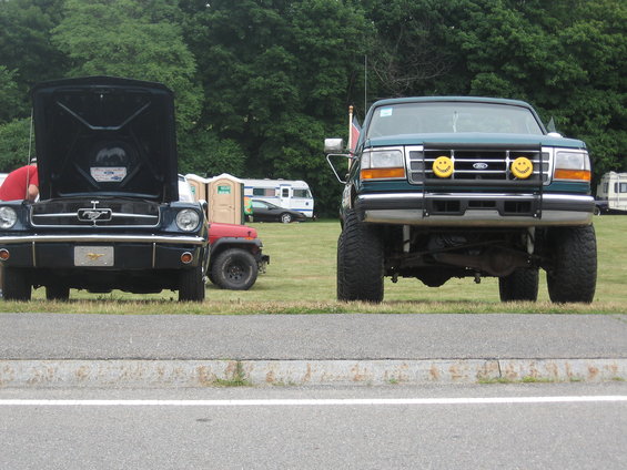 green lifted Ford truck with smiley face lights, black classic car with hood up, and red Jeep