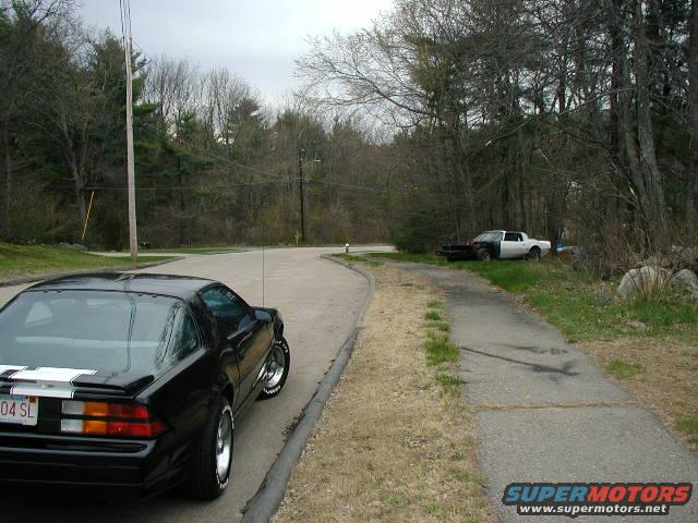 Black 1988 Chevrolet Camaro parked on a road, with a white pickup truck in the background