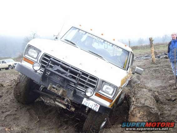 White 1978 Ford Bronco stuck in mud with a winch on the front bumper. Another vehicle is visible in the background