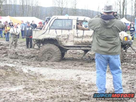 Muddy off-road vehicle stuck in a mire with people around