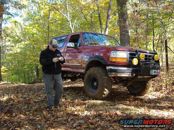 Man with camera next to red 1996 Ford Bronco in wooded area