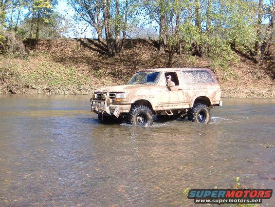 1996 Ford Bronco driving through a river, covered in mud