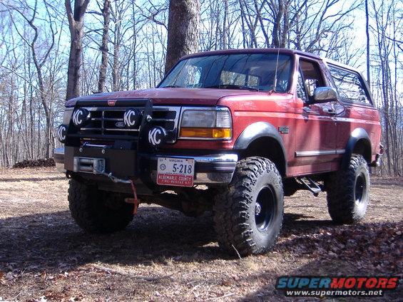Red Ford Bronco with aftermarket grille guard, winch, and KC lights