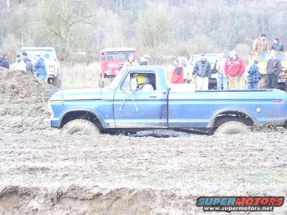 Blue pickup truck stuck in mud with people watching in the background