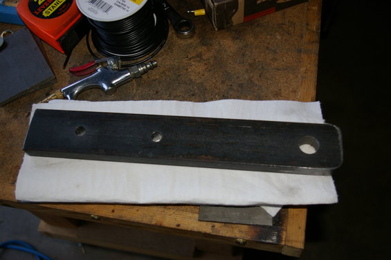 Dark metal clevis mount with three holes, resting on white paper