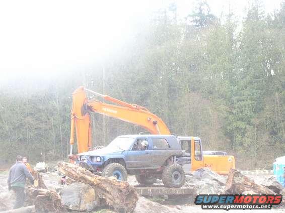 Blue SUV with large tires and lifted suspension next to an excavator