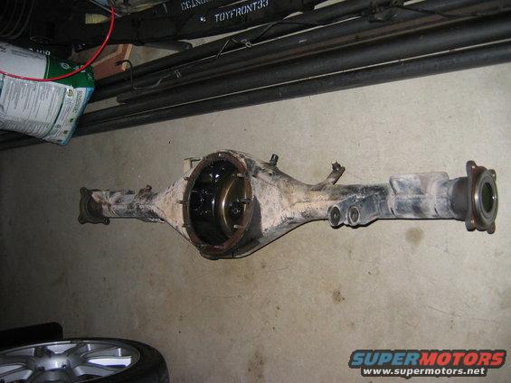 Rear differential assembly on concrete floor. Some pipes and a bag are in the background. Supermotors.net logo visible