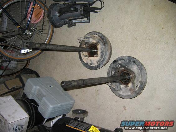 Two axle shafts with brake drums on a concrete floor next to a bicycle wheel and storage containers