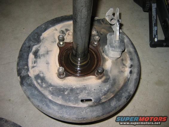 Rear axle hub with brake drum, showing bearing and mounting bolts. A metal shaft extends upwards