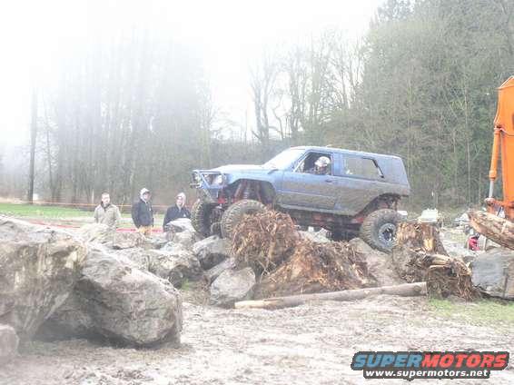 Blue off-road SUV with large tires climbing over rocks and debris