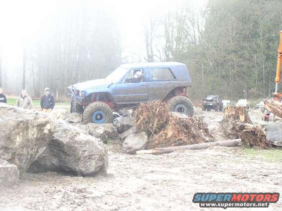 Blue off-road SUV with large tires navigating a muddy obstacle course