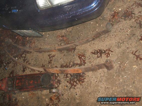 Two rusty leaf springs and a dark blue car fender with a headlight visible