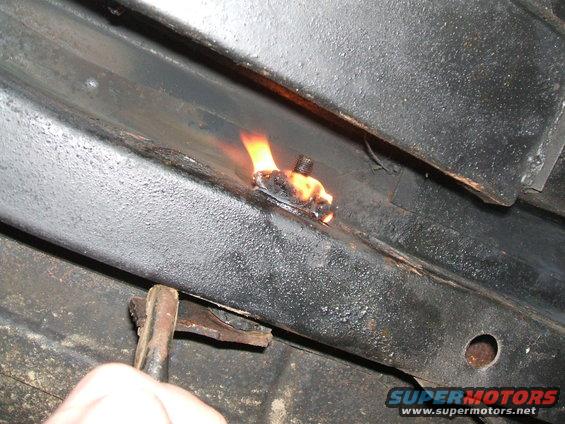 Frame rail with bolt being heated by torch, part of rear suspension repair