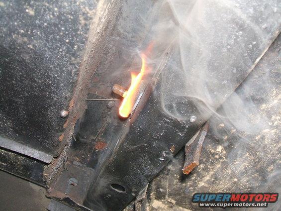 Close-up of a bolt being welded, with flame and smoke, on a rusty metal frame