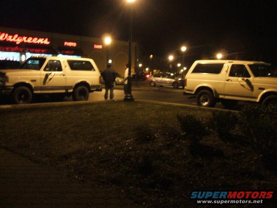 Two white 1990 Ford Broncos parked at night in front of a Walgreens