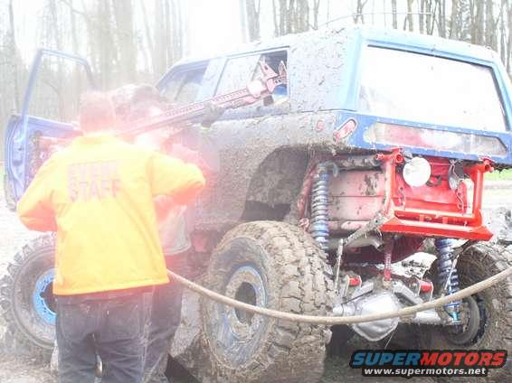 Muddy off-road vehicle with people, one wearing a yellow jacket with 'STAFF' visible