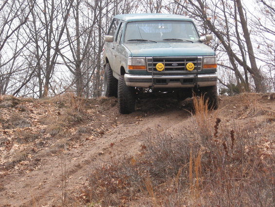 Teal 1996 Ford Bronco with smiley face headlights driving on a dirt hill