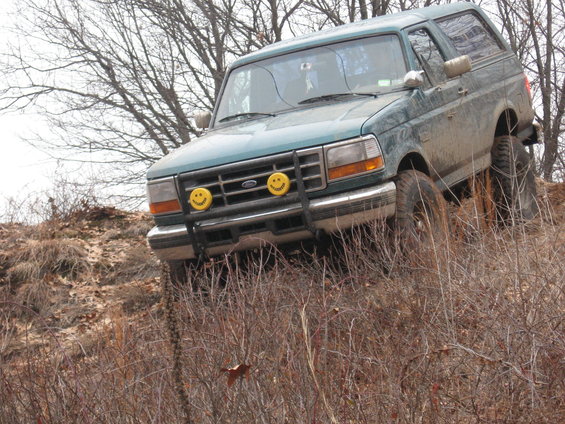 Green 1996 Ford Bronco climbing a dirt hill with trees in the background