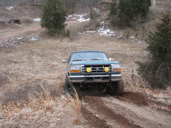 Green 1996 Ford Bronco driving on a dirt track with two yellow smiley face lights on the front bumper