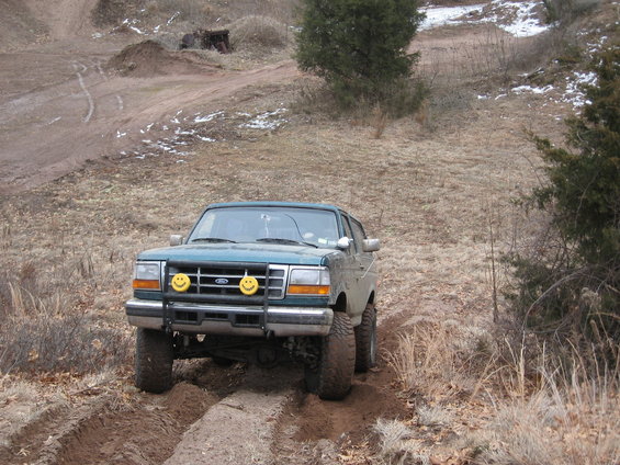 Green Ford Bronco with smiley face fog lights driving on a dirt path