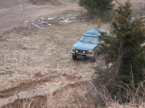1996 Ford Bronco driving on a muddy, dry grass field with trees