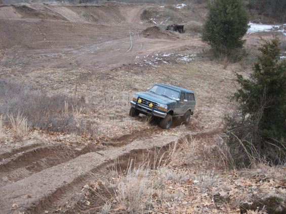 Green 1996 Ford Bronco driving off-road on a dirt track with tire tracks visible