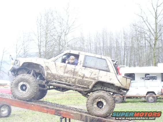 muddy off-road SUV on ramp, another SUV and trailer in background
