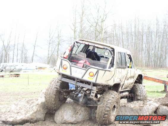Modified off-road SUV with large tires stuck on rocks in mud. Roll cage visible
