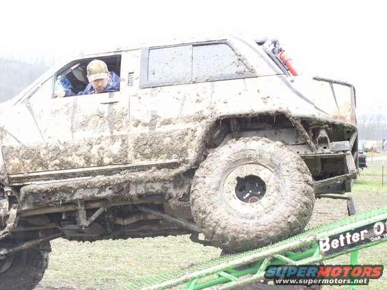Mud-covered off-road vehicle with large tires on a ramp, driver visible inside