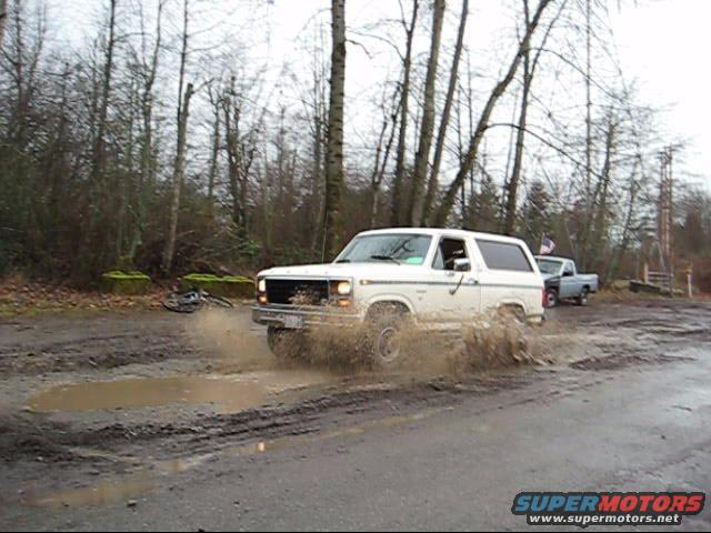 White 1980 Ford Bronco splashing through mud puddle, side view