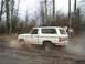 1980 Ford Bronco - A white 1980 Ford Bronco kicks up mud as it drives through a wooded area.