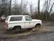 1980 Ford Bronco - A white Ford Bronco kicks up mud as it drives through a wet, wooded area.
