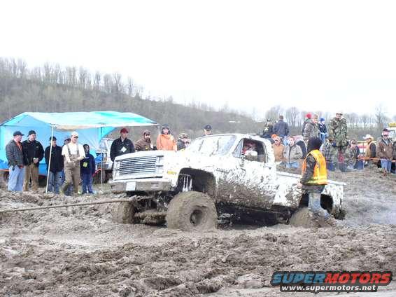 Mud-covered pickup truck stuck in deep mud, with spectators watching