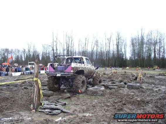 Muddy lifted truck with roll cage in a mud pit with tires scattered around