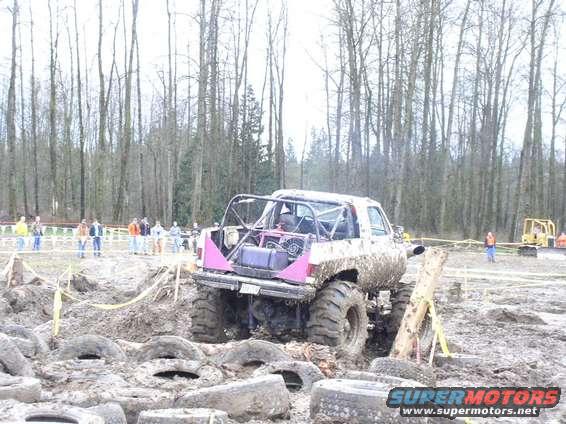Mud-covered off-road vehicle with roll cage and large tires, viewed from the rear