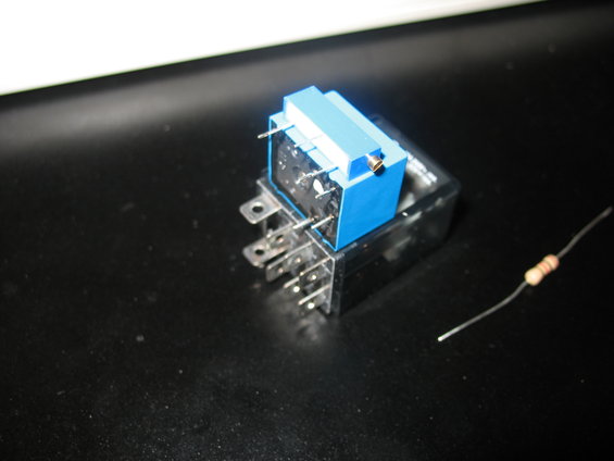 Blue and black automotive relay with metal pins, next to a small resistor with brown and beige bands