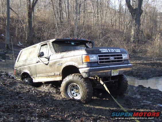 Mud-covered Ford Bronco stuck in mud, front grille visible