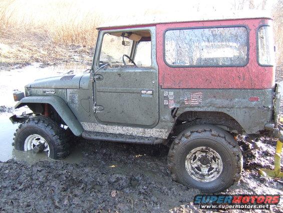 Mud-splattered green and red Toyota Land Cruiser stuck in mud, side view